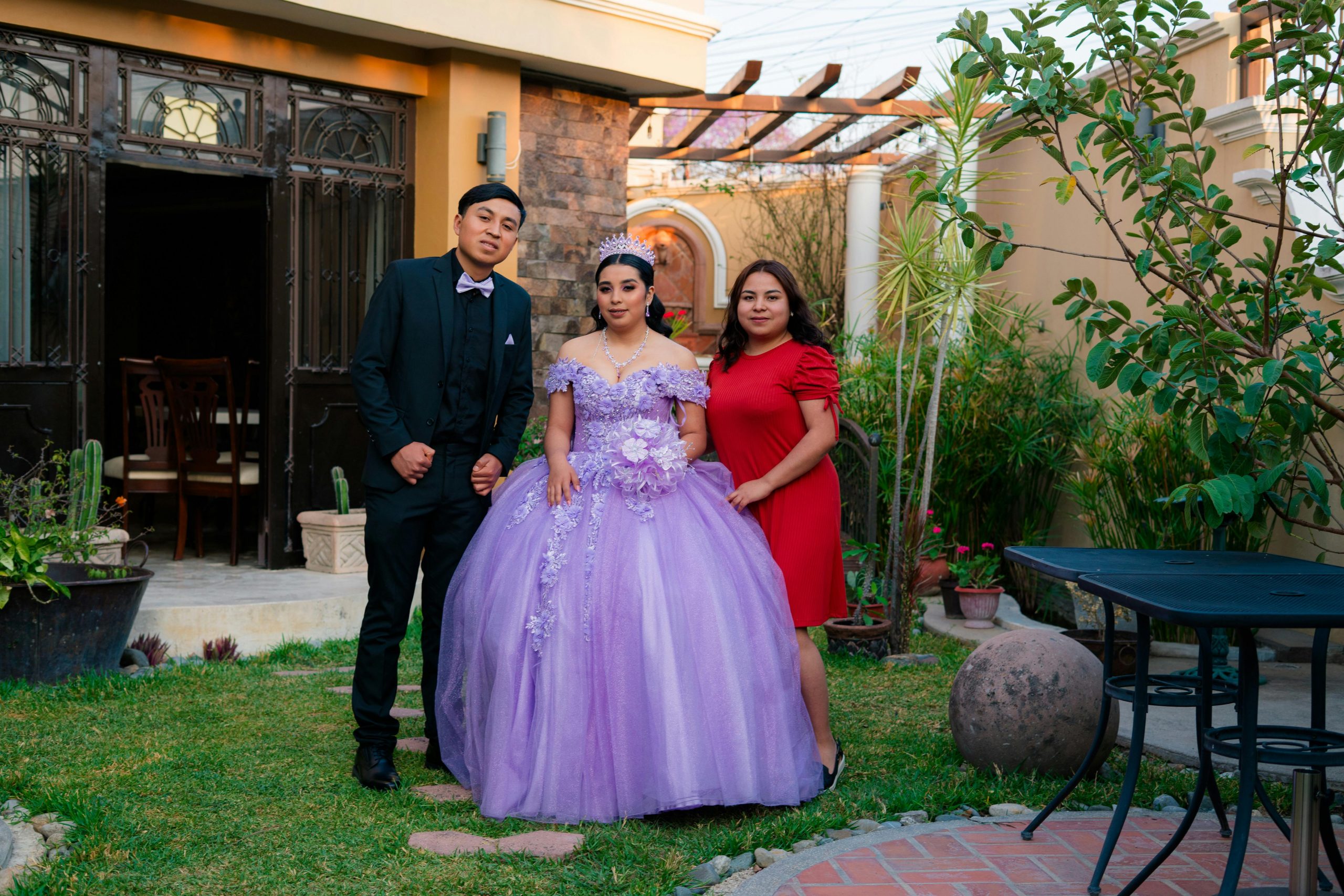 Young woman in purple gown for quinceañera with family in a garden setting.